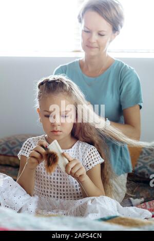 Spazzole madre lunghi capelli biondi di sua figlia sul letto e la figlia spazzole capelli della sua bambola Foto Stock