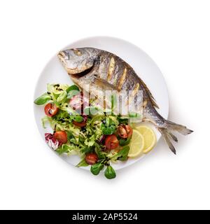 Dorada grigliata di pesce sulla piastra bianca con insalata fresca e pezzi di limone. Fotografia di cibo Foto Stock