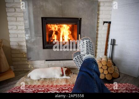 Concetto di Hygge con gambe di uomo in calze di lana vicino al caminetto Foto Stock