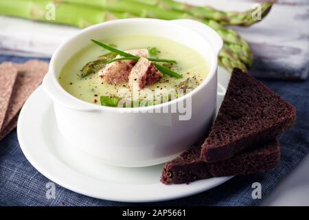 Zuppa di asparagi con pane nero in bianco ciotola closeup. Fotografia di cibo Foto Stock