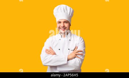 Lo Chef Positivo Uomo Sorridente A Camera Crossing Hands, Sfondo Giallo Foto Stock