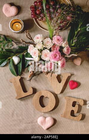 San Valentino o un matrimonio romantico impostazione tabella con lettere in legno amore, ago cuori feltrato, bouquet di rose rosa e uve rosse sul naturale l Foto Stock