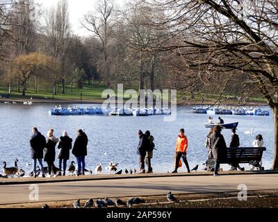 Vista attraverso la serpentina, Hyde Park, Londra con pedalò a noleggio e persone che alimentano gli uccelli in un Sabato freddo nel mese di gennaio Foto Stock