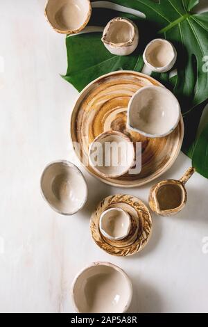 Varietà di vuoto diversi piatti in ceramica, bocce, brocche e piatti esotici su foglie di monstera su marmo bianco dello sfondo. Laici piana, spazio Foto Stock