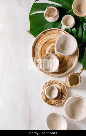 Varietà di vuoto diversi piatti in ceramica, bocce, brocche e piatti esotici su foglie di monstera su marmo bianco dello sfondo. Laici piana, spazio Foto Stock