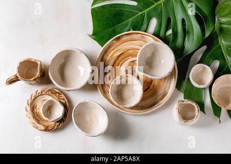 Varietà di vuoto diversi piatti in ceramica, bocce, brocche e piatti esotici su foglie di monstera su marmo bianco dello sfondo. Laici piana, spazio Foto Stock