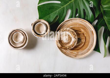 Varietà di vuoto diversi piatti in ceramica, bocce, brocche e piatti esotici su foglie di monstera su marmo bianco dello sfondo. Laici piana, spazio Foto Stock