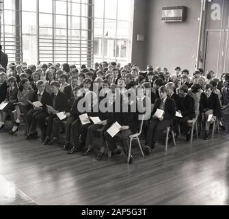1965, i bambini storici della scuola secondaria che si siedono insieme in una sala della scuola per l'assemblea, Inghilterra, Regno Unito. Foto Stock
