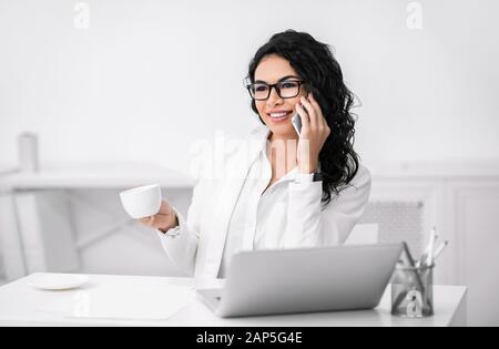 Donna d'affari ispanica sorridente che parla sul suo cellulare Foto Stock