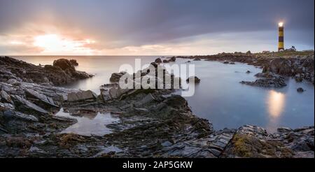 Twilight inizia a cedere alla luce del giorno al faro di St. Johns Point. Costa rocciosa con acqua e cielo sfocati, fotografia a lunga esposizione Foto Stock