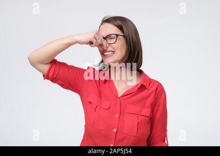 L'uomo caucasico maturo nei vetri e nei tappi rossi della camicia vicino il naso con le dita ritiene il profumo sgradevole soffre dal pustench che pone isolato sullo studio grigio Foto Stock