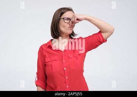 L'uomo caucasico maturo nei vetri e nei tappi rossi della camicia vicino il naso con le dita ritiene il profumo sgradevole soffre dal pustench che pone isolato sullo studio grigio Foto Stock