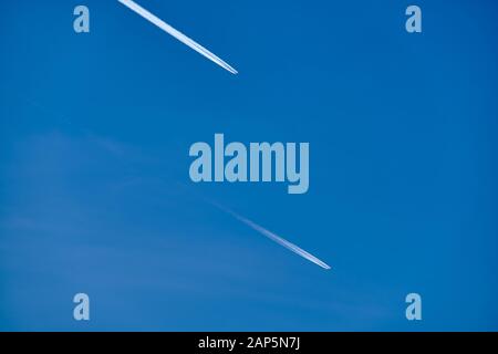 Profondo blu del cielo con il bianco di scie di condensazione di due aeroplani volare alto fino all'aria. Visto in Germania nel mese di dicembre Foto Stock