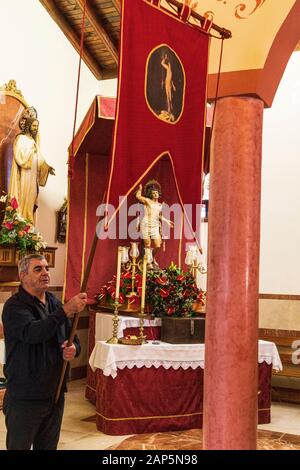 Un uomo tiene alto il vessillo della santa di fronte alla statua di San Sebastian in chiesa nel giorno della locale fiesta in La Caleta, Costa Adeje Foto Stock