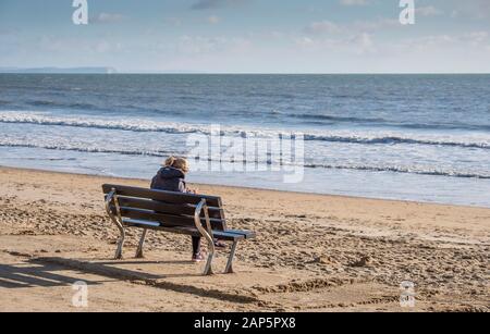 Bournemouth Beach con una persona seduta da sola sul lungomare mentre si utilizza un telefono cellulare in inverno. Foto Stock