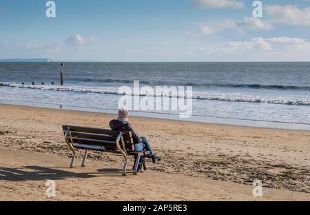 Una persona seduta da sola sulla Promenade di Bournemouth che guarda solo in inverno Foto Stock