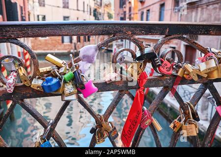 Rosso a forma di cuore, combinazione e altri lucchetti sul ponte di Venezia, Italia. Giornata di sole, edifici storici e il canale sullo sfondo Foto Stock