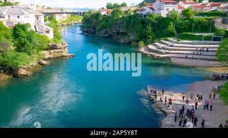 Mostar, BOSNIA-ERZEGOVINA, aprile 2019: Persone che si trovano sulla riva del fiume Neretva e che per lo più scattano foto del Ponte Vecchio a Mostar. Foto Stock