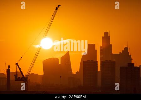 Il sole tramonta dietro di gru a torre e la skyline di Londra nel distretto finanziario di Londra. Foto Stock