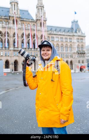 uomo in impermeabile giallo con grande fotocamera dslr a piazza della città Foto Stock