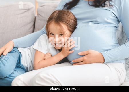 Cute bambina che ascolta di aspettarsi mamma pancia Foto Stock