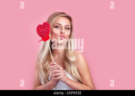 Ragazza bionda felice che tiene un lollipop rosso a forma di cuore. San Valentino Foto Stock