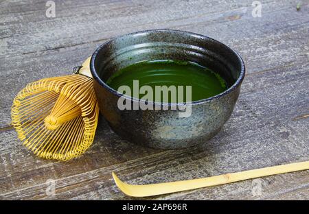 Concetto di preparazione del tè Matcha: Primo piano del set isolato per la preparazione del tè verde Matcha: Un bicchiere e un cucchiaio di bambù, recipiente in ceramica su vecchio tavolo in legno Foto Stock