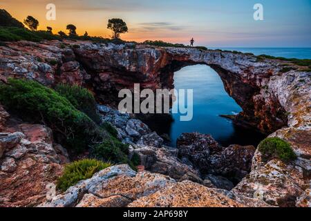 Silhouette di uomo su Cala Varques, ponte naturale sull'acqua di mare vicino Portocolom, Maiorca Foto Stock