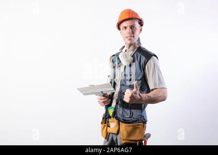 Builder con una spatola. E mostra Thumbs up. In abiti da lavoro e di elmetto. Su uno sfondo grigio chiaro. Foto Stock