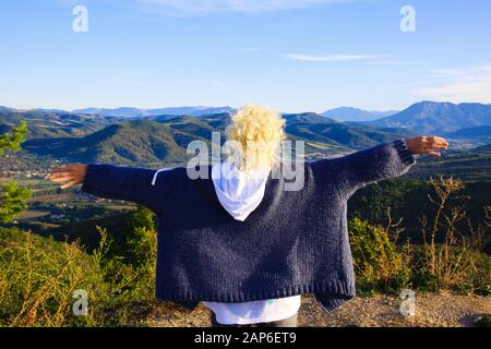 Vista su una donna isolata con capelli ricci biondi e braccia spalmabili su un altopiano che si affaccia su una valle infinita con catena montuosa - Grand Canyon du Verdon, p. Foto Stock