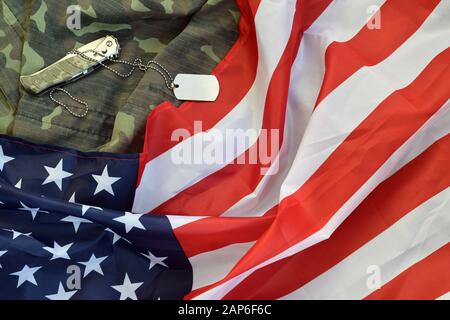 Gettone e coltello per il cane dell'esercito si trova sulla vecchia uniforme camouflage e sulla bandiera degli Stati Uniti piegata. Sfondo per il design Veterans Day Foto Stock