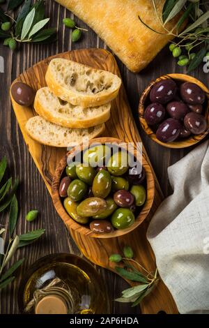 Olive e olio d'oliva e ciabatta sul tavolo di legno. Foto Stock