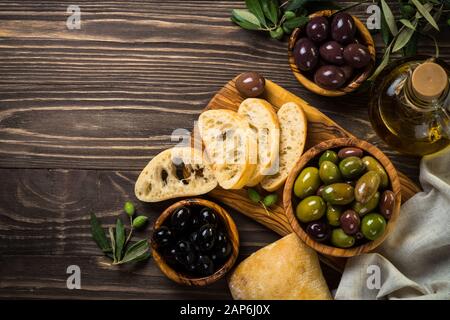 Olive e olio d'oliva e ciabatta sul tavolo di legno. Foto Stock