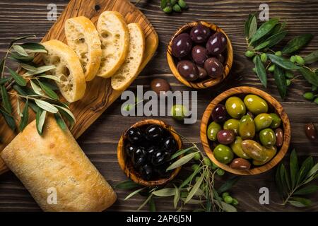 Olive e olio d'oliva e ciabatta sul tavolo di legno. Foto Stock