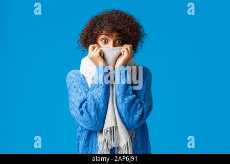 Stupida paura e arrossata cute afroamericana donna con taglio di capelli afro, nascondendo il viso dietro sciarpa, fissando occhi pop fotocamera sorpreso o leggermente Foto Stock