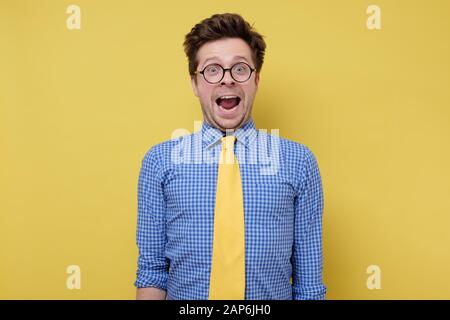 Goofy giovane uomo con lo stile divertente dei capelli che è eccitato pieno di gioia sul muro giallo. Foto Stock