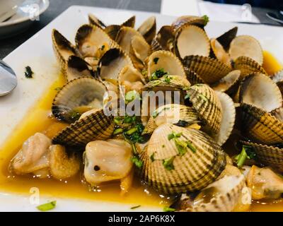 Fresche le vongole cotte con erbe e aglio su una piastra bianca Foto Stock