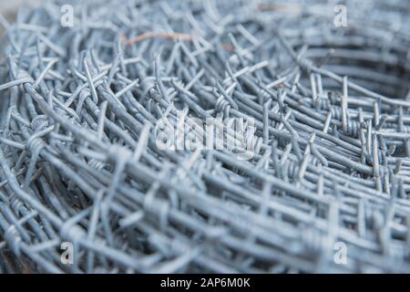 Primo piano su un rotolo di pile di nuovo filo spinato lucido per recinzione recinto. Protezione della sicurezza applicazione della legge. Carcere reato penale bloccato. Foto Stock