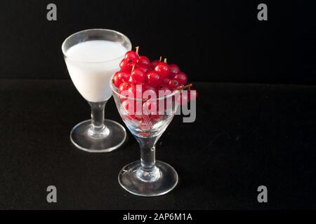 piccoli bicchieri pieni di cibo sano, ribes rosso e latte su sfondo nero Foto Stock