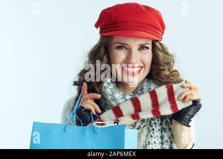 Ritratto di felice elegante 40 anni donna con lunghi capelli bruna in maglione, sciarpa e cappello rosso e blu con shopping bag mostra gli acquisti contro wi Foto Stock