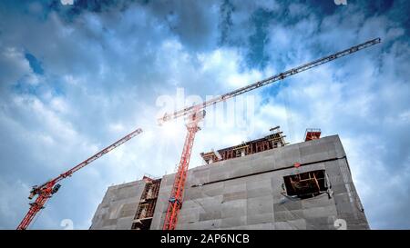 Un team di lavoratori sta lavorando e una grande gru sul moderno edificio a più piani per completare il piano. In una giornata limpida Foto Stock