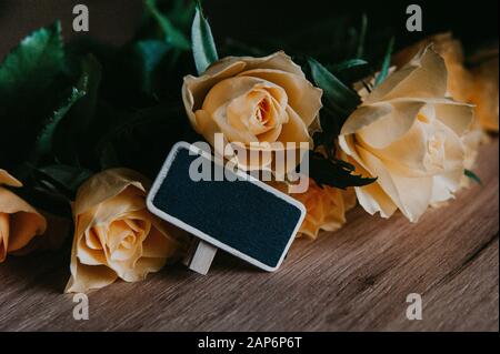 Piccola lavagna nera e rose gialle su un tavolo di legno. Mockup, spazio per il testo. Compleanno, primavera, Pasqua, festa della mamma, 8 Marzo concetto. Foto Stock