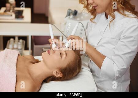 Bella donna che riceve ultrasuoni viso scrubbing e massaggio. Cosmetologia e cura della pelle del viso. Trattamento viso, pulizia viso. Elettronico Foto Stock