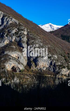 Grotta di Niaux e strada di accesso con nevoso Mont Olmes dietro, visto da tutta la valle, Ariege, Pirenei francesi, Francia Foto Stock