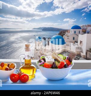 Insalata greca contro la famosa chiesa nel villaggio di Oia - Santorini Island in Grecia Foto Stock