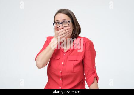 Una giovane donna europea seria che copre la bocca con entrambe le mani mantenendo un segreto. Studio Foto Stock