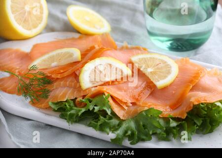 Fette di Salmone affumicato con lattuga e fette di limone su un tagliere Foto Stock