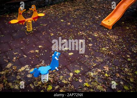 Parco giochi per bambini vuoto con giocattoli colorati e foglie a terra dopo la pioggia. Foto Stock