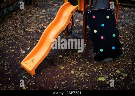 Parco giochi per bambini vuoto con giocattoli colorati e foglie a terra in autunno dopo la pioggia. Foto Stock