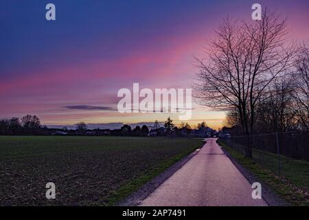 Bella spettacolare viola e rosa nube e cielo dopo tempesta e pioggia su campo agricolo e strada sulla campagna in Germania. Foto Stock